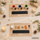 Composición navideña elegante con dos bandejas personalizadas de madera, una para Papá Noel y otra para los Reyes Magos, presentadas sobre un fondo claro con decoración festiva en tonos neutros. Velas, ramas de abeto, luces cálidas y detalles de madera cr