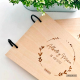 Libro de firmas con tapas de madera de haya natural grabadas al láser personalizada con los nombres de Alberto y María y la fecha del enlace, tiene una cenefa decorativa al rededor de estos datos y anillas negras.